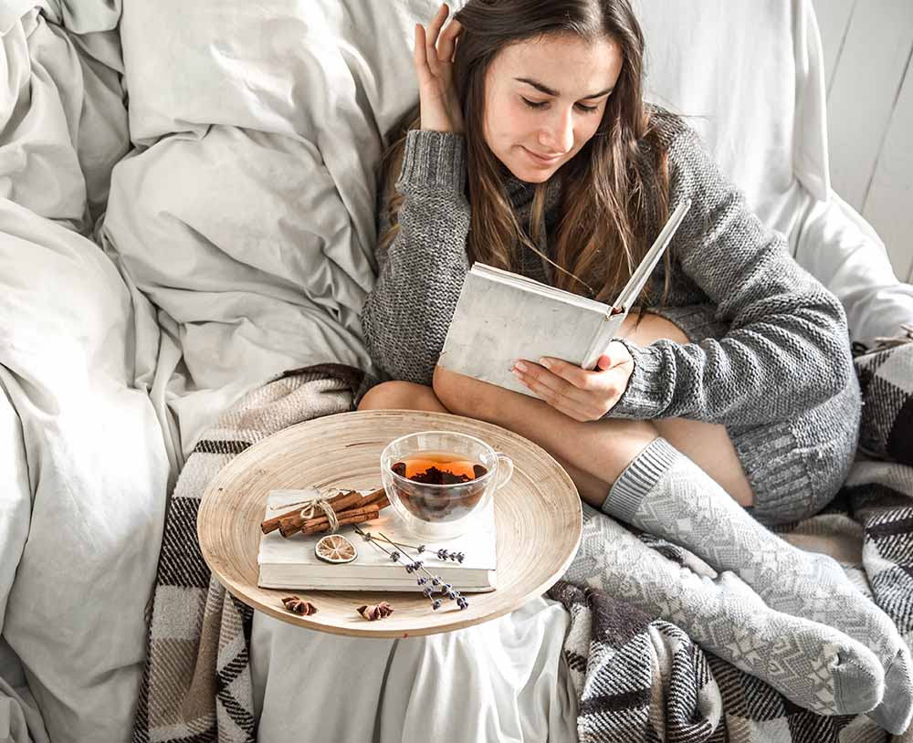 roztomilá dívka sedí komfortně na židli s čajem a čte si knihu